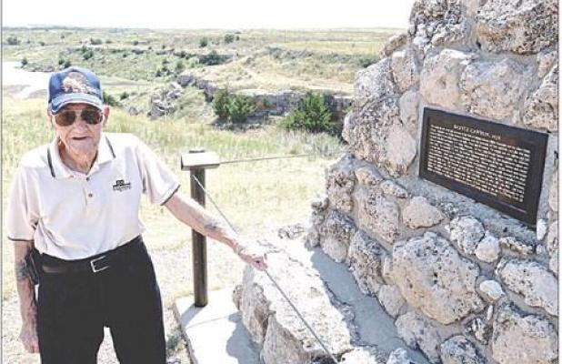With Battle Canyon in the background, Dennie Siegrist stands by the monument that gives a brief description of events that occurred at the historic site. (Record Photo)