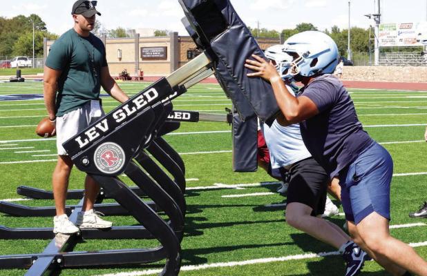 SCHS assistant coach Drew Kite encourages the linemen as they work out on the blocking sled during the opening day of practice on Monday. (Record Photo)