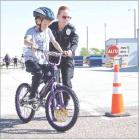 Eight-yearold Pierce Goode, Scott City, navigates the bicycle course with assistance from Scott City Police Sgt. Whitney Savolt. Bicycle safety was one of the activities held in Palmer Park during the Safe Kids Day event which followed the annual ‘Go Fa