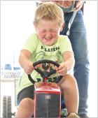 Five-year-old Ryker Olds grimaces as he completes a full pull in the kids pedal tractor pulling competition held during the Scott County Fair. (Record Photo) just a little farther