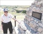 With Battle Canyon in the background, Dennie Siegrist stands by the monument that gives a brief description of events that occurred at the historic site. (Record Photo)