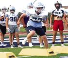 (Above) Playing under the lights during three of their summer camp sessions, senior Brooks Bailey makes a leaping tackle of a tackling donut. (Right) Sophomore Reid Felker goes through conditioning and footwork drills. (Record Photos) fall is (almost) in the air