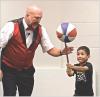 Juggler Richard Holmgren gets some assistance from Dexter Wiebe who balances a spinning basketball on a stick during the “Flying Debris” program held at the Scott County Library on Tuesday morning. (Record Photo)
